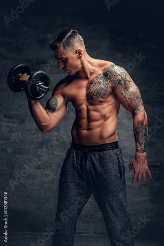 Athletic male with tattoo on his chest doing biceps workouts with dumbbell.