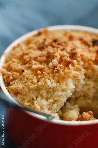 Close-up of an apple crumble pie in a red bowl on a blue napkin. Macro photography.