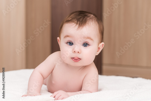 adorable baby girl lying on her stomach on soft blancket and show tongue. portrait of cute baby girl with blue eyes and long eyelashes