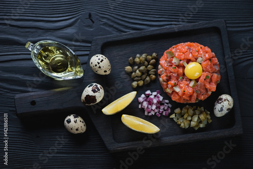 Black wooden serving tray with salmon tartar, studio shot, high angle view