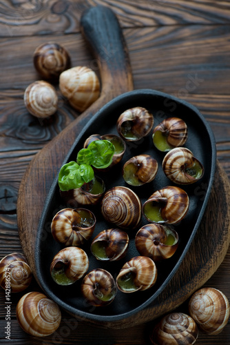 Frying pan with escargot snails with garlic butter, rustic wooden surface, selective focus