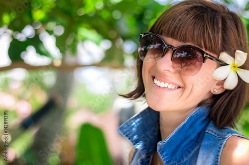 Portrait Young beautiful tropical woman on summer vacation in asia, Bali. Relaxing on tropical beach, sea landscape and gree tropical background, slim tanned body, travel alone, short hair.