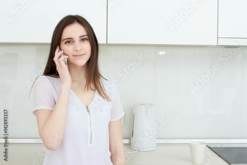 Brunette housewife in white in the kitchen talking on the mobile phone