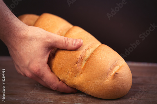 male hand holding bread loaf on the wonderful brown wooden background