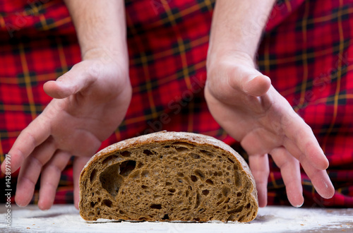 male hand under bread loaf on the wonderful red checkered background
