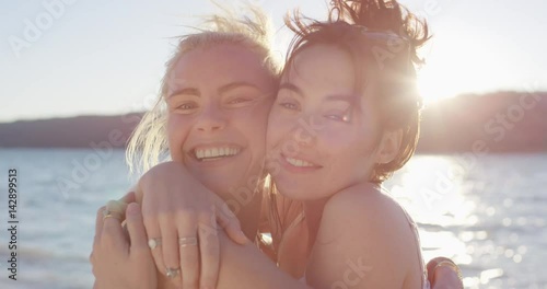 Beautiful young woman giving teenage girl friend kiss on cheek hugging each other on vacation at sunset magic hour