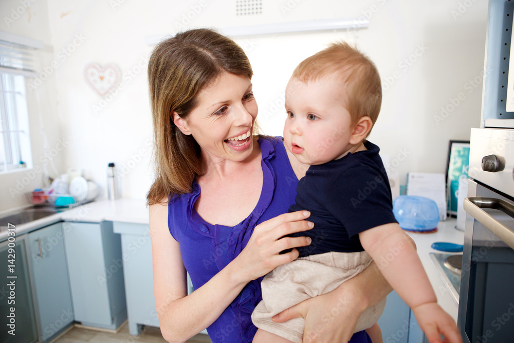beautiful young woman carrying her baby boy in kitchen beautiful young woman carrying her baby boy in kitchen