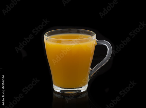 Glass with yellow juice on a black background with shadow