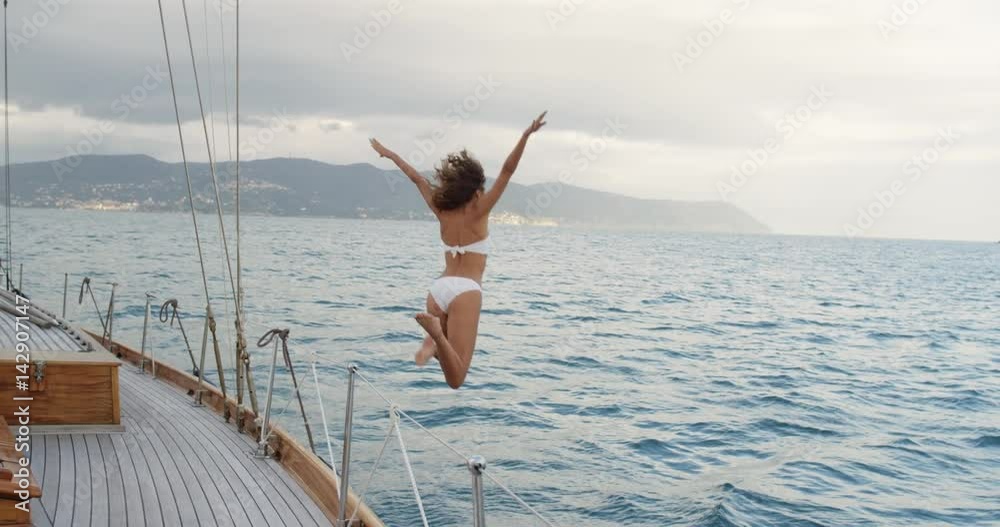 Beautiful girl jumping into blue sea from luxury wooden sailboat fun happy lifestyle ocean vacation travel Beautiful girl jumping into blue sea from luxury wooden sailboat fun happy lifestyle ocean vacation travel
