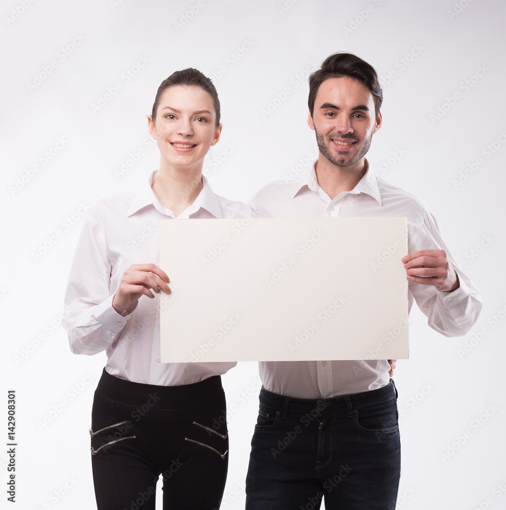 Young happy couple showing presentation pointing on placard over gray background Young happy couple showing presentation pointing on placard over gray background