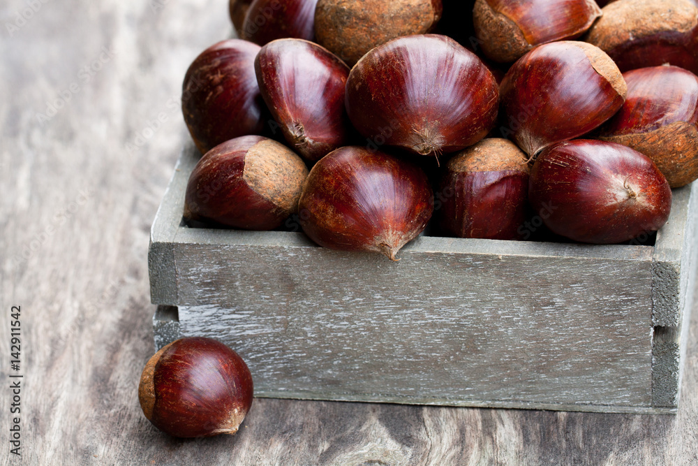 Obraz premium fresh raw chestnuts in a wooden box on wooden background