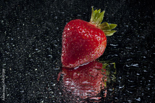 red wet strawberry on reflective surface 