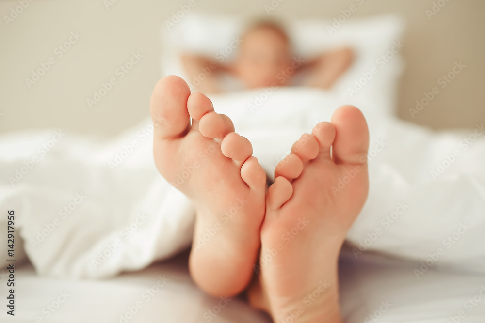 Beautiful feet of a small child lying under a white blanket, close-up