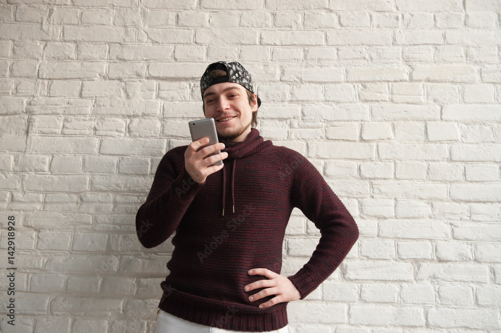 Obraz premium smiling young man wearing cap looking into smartphone in his hand