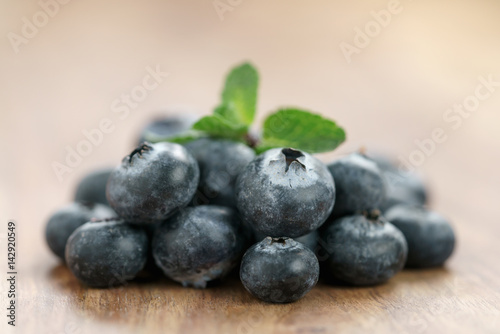 heap of fresh garden blueberries with mint leaves on wood table, closeup photo
