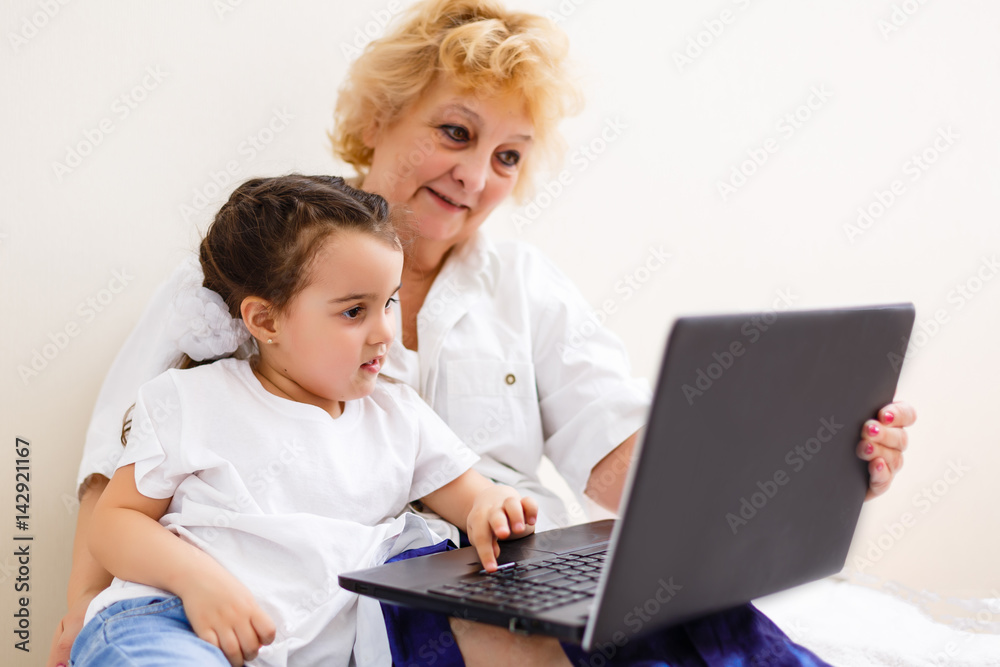cheerful little girl and grandma using laptop computer at home