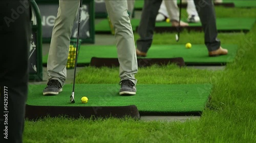 People have training on the golf driving range. Legs and clubs close shot.