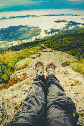 Legs of traveler sitting on a high mountain top in travel. Freedom concept