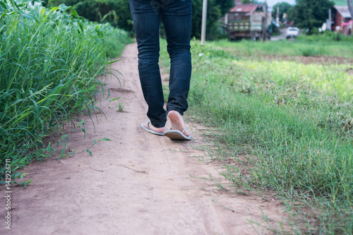 Close up young adult man walking away on path through the grass field in Thailand. Asian style