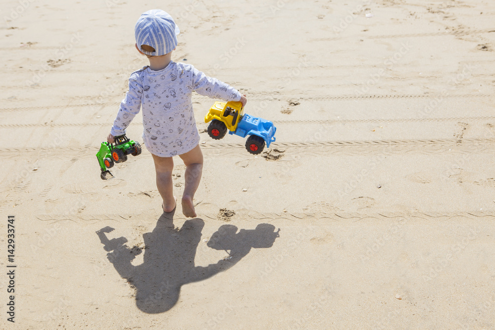 Fototapeta premium Baby boy walking with toys at the beach