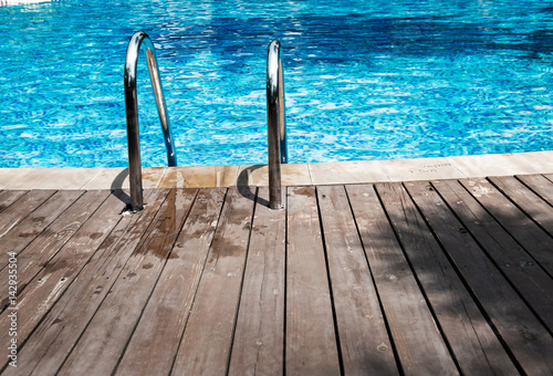 Swimming pool with stair and wooden deck at hotel.