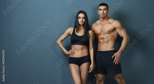 Young couple with a sports body posing against the wall background
