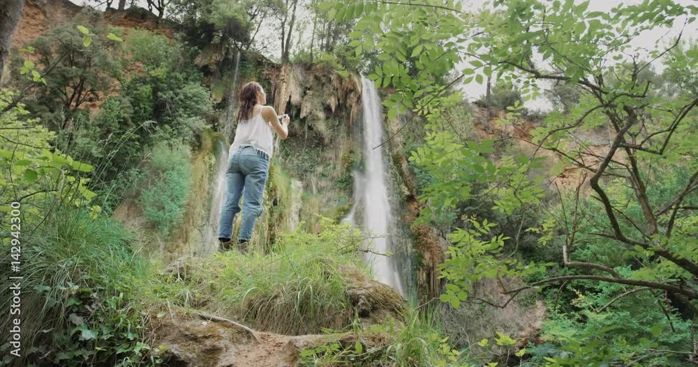 Young woman taking photograph with smart phone at base of hidden waterfall girls in nature enjoying carefree vacation outdoors adventure Young woman taking photograph with smart phone at base of hidden waterfall girls in nature enjoying carefree vacation outdoors adventure