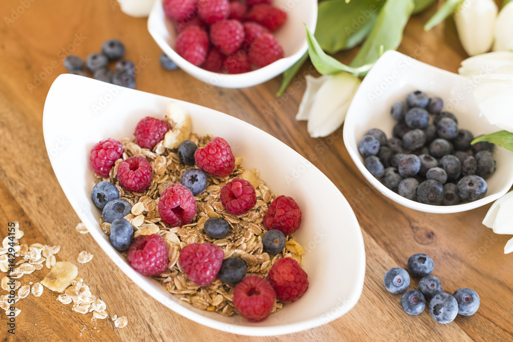 Breakfast with granola or muesli und fresh raspberries and blueberries on a wood table Breakfast with granola or muesli und fresh raspberries and blueberries on a wood table