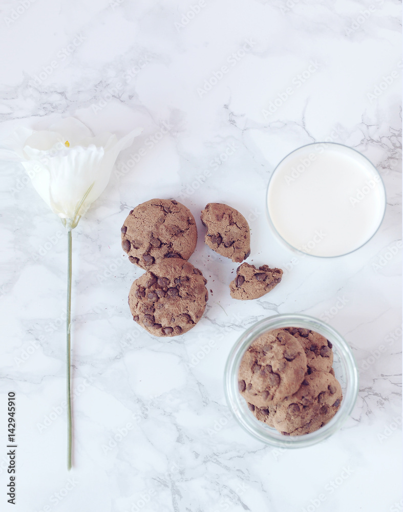 Crisp chocolate cookies with a glass of milk and white flower on marble background. Flat lay. Top view