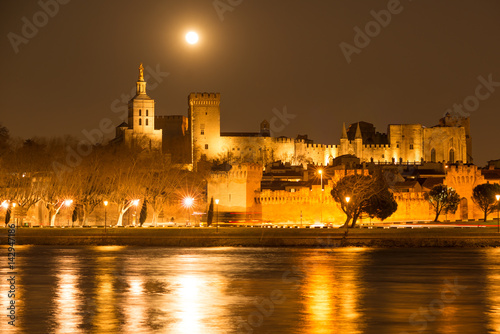 Nighttime panorama of historic Palace of the Popes in Avignon with rising full moon, Provence, France