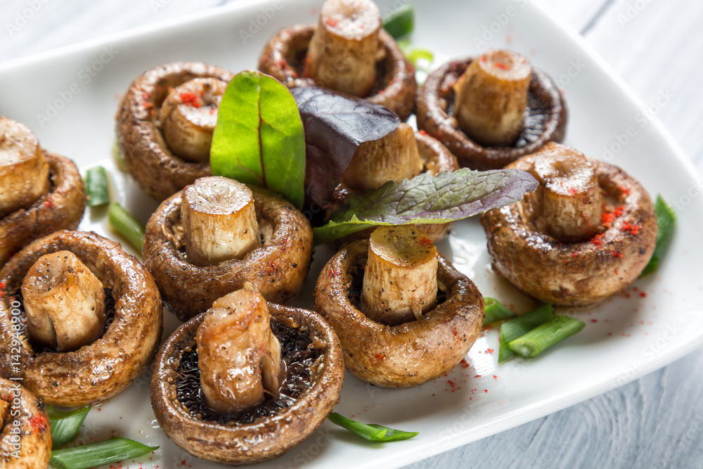 Grilled champignon white mushrooms on white plate with herbs and spices. Close up with selective focus Grilled champignon white mushrooms on white plate with herbs and spices. Close up with selective focus
