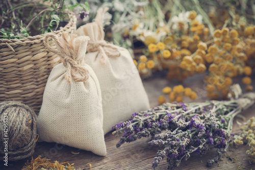 Sachets filled with dried medicinal herbs and  bunches of healing herbs on wooden board. Herbal medicine. Retro toned. photo