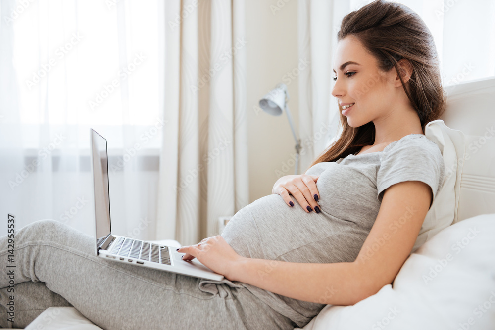 Pregnant woman using laptop on bed in bedroom Pregnant woman using laptop on bed in bedroom