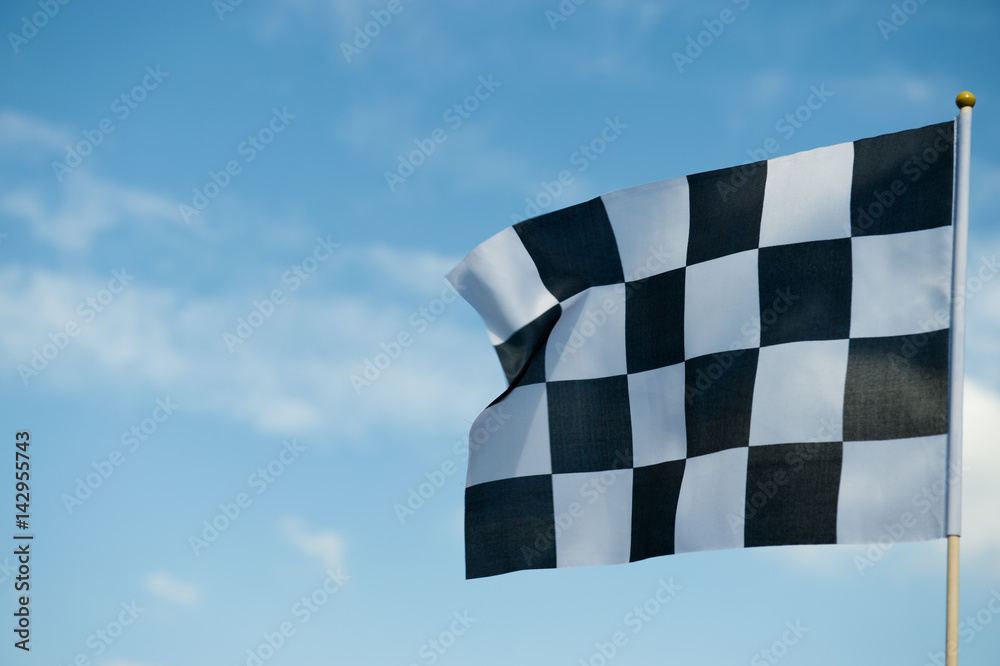 checkered race flag waving on blue sky.