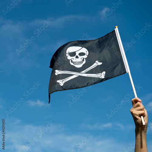 skull flag in hand waving on blue sky background.