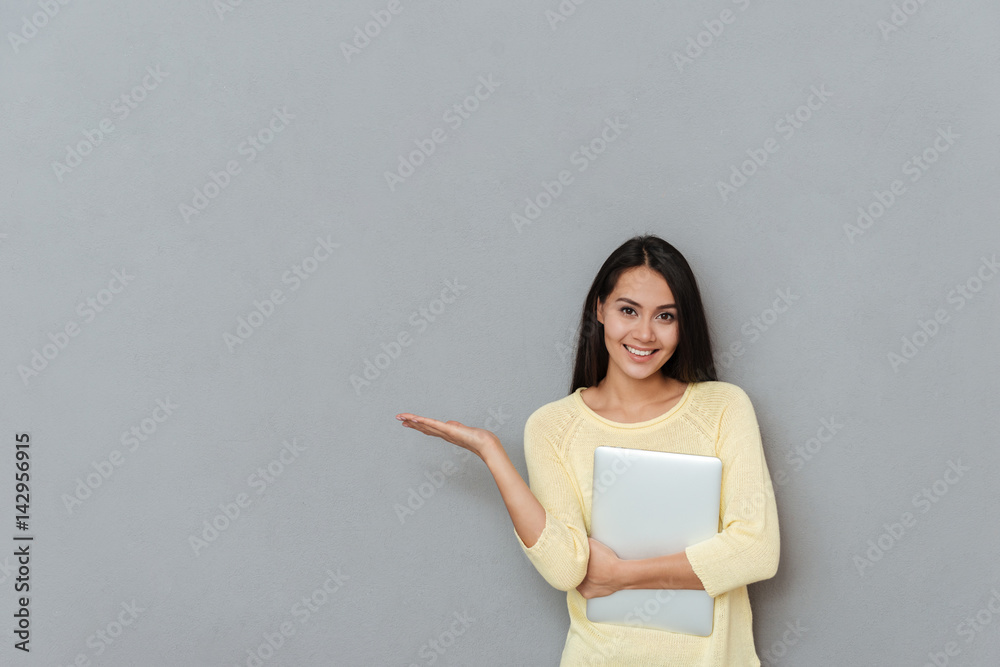 Cheerful woman with laptop standing and holding copyspace on palm Cheerful woman with laptop standing and holding copyspace on palm