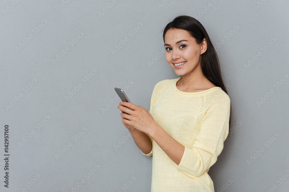 Cheerful pretty young woman standing and using cell phone Cheerful pretty young woman standing and using cell phone