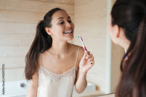 Woman looking at the mirror and brushing teeth in bathroom