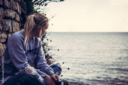 Thoughtful lonely young woman tourist with closed eyes thinking during her travel sitting on seashore in retro vintage style