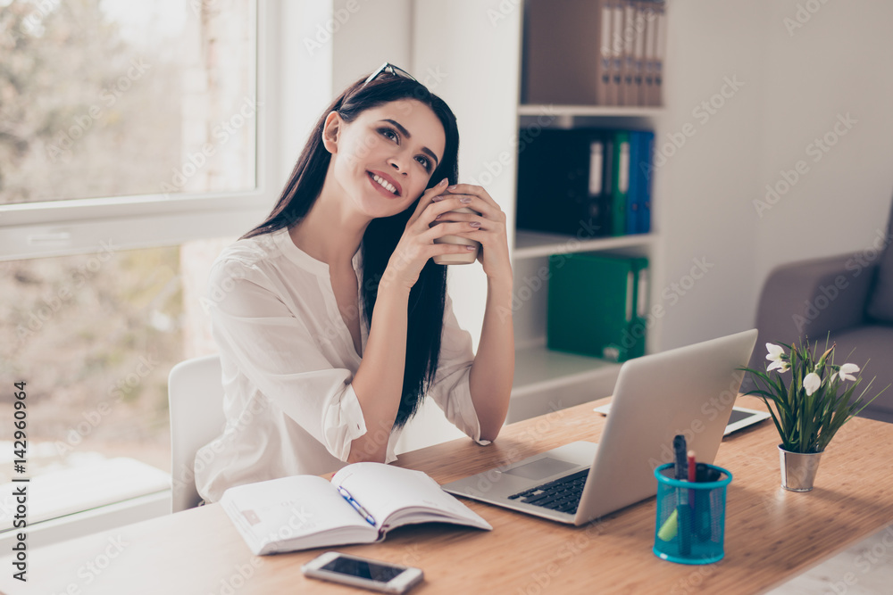 Portrait of young pretty woman with beaming smile sitting at the table drinking coffee and dreaming about weekend Portrait of young pretty woman with beaming smile sitting at the table drinking coffee and dreaming about weekend