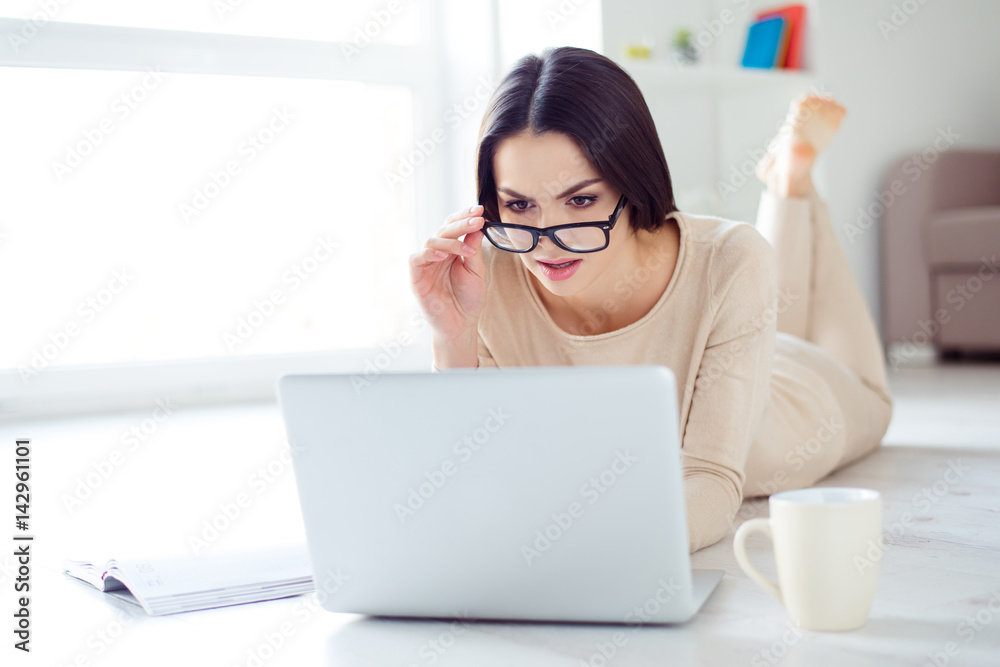 Freelance concept. Young successful woman in glasses at a loss working at home while lying on the floor with laptop. . Freelance concept. Young successful woman in glasses at a loss working at home while lying on the floor with laptop. .