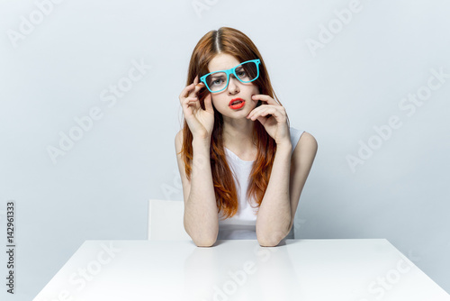 red-haired woman in blue glasses and with red lips sits at the table