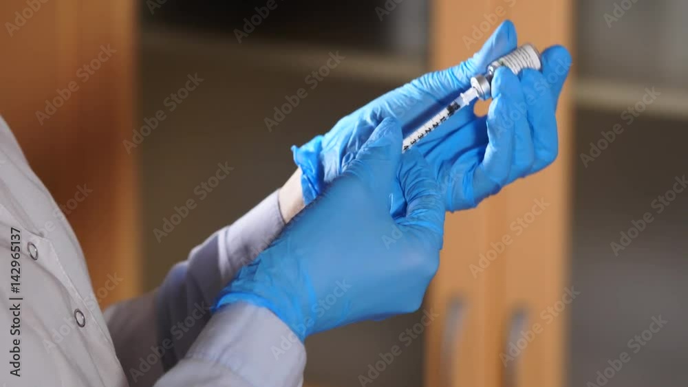 The doctor of the private clinic, dressed in a robe and anti-bacterial gloves, releases excess air from the syringe with the medicine, so that only the medicine is administered to the patient's skin. The doctor of the private clinic, dressed in a robe and anti-bacterial gloves, releases excess air from the syringe with the medicine, so that only the medicine is administered to the patient's skin.