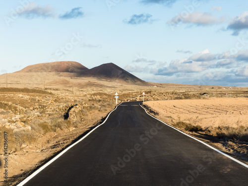 Lonely, remote road at sunset running trough a deserted landscape with volcano mountains on the Canary Islands.