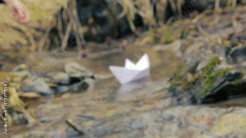 Woman's hand putting paper boat on the water and pushing it away. Paper boats adrift in the river. Origami paper boat sailing from winter to spring. Kazakhstan