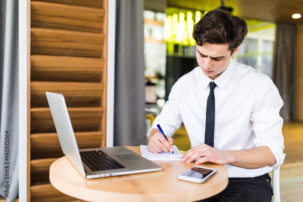 Attractive businessman is using a laptop, talking on the mobile phone and smiling while working Attractive businessman is using a laptop, talking on the mobile phone and smiling while working