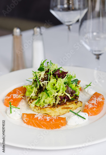 beautifully prepared dish consisting of slices of fresh atlantic Salmon fillet  lightly fried potato cake  mozzarella chunks and salad. All served on a clean white plate.