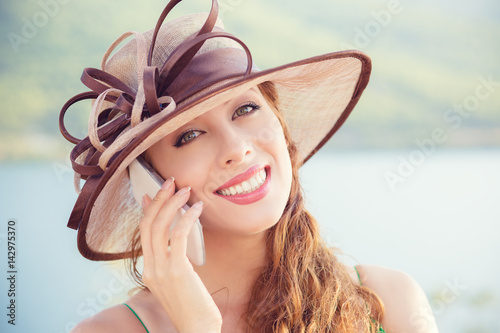 Euphoric woman talking to her smart phone at the sea. Lady in hat at mobile by the sea. photo