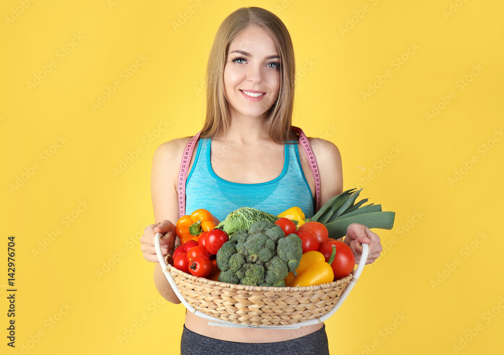 Young beautiful woman holding basket with vegetables on yellow background Young beautiful woman holding basket with vegetables on yellow background