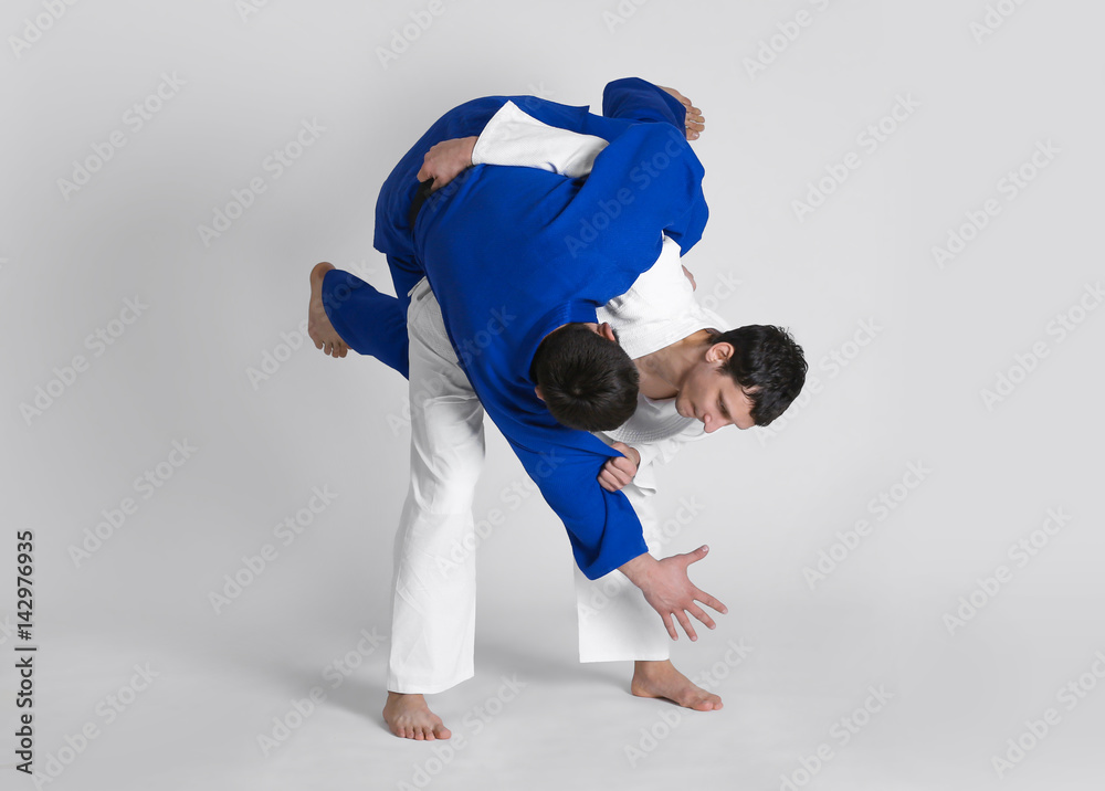 Fototapeta Young sporty men practicing martial arts on light background